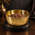 AURORA hand-hammered brass pet food bowl filled with kibble, moody studio setting with a brass vase