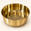 Golden Retriever lying near the DUNE smooth-finish brass pet food bowl on a woven mat with an olive branch