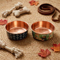 Medium and large DAMASK copper pet bowls side by side on a jute rug with a leather leash and fall leaves