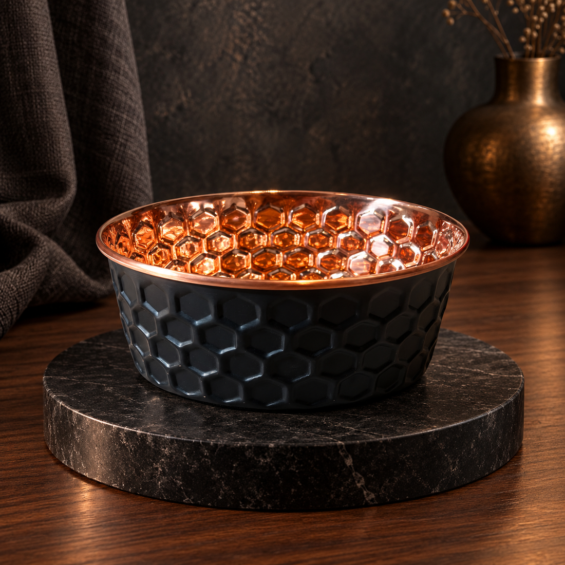 ONYX black diamond-hammered copper pet bowl on a dark marble stand with a brass vase, moody studio setting