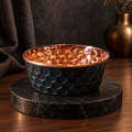 ONYX black diamond-hammered copper pet bowl on a dark marble stand with a brass vase, moody studio setting