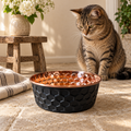 Tabby cat sitting beside the ONYX black diamond-hammered copper pet bowl near a wooden stool with wildflowers