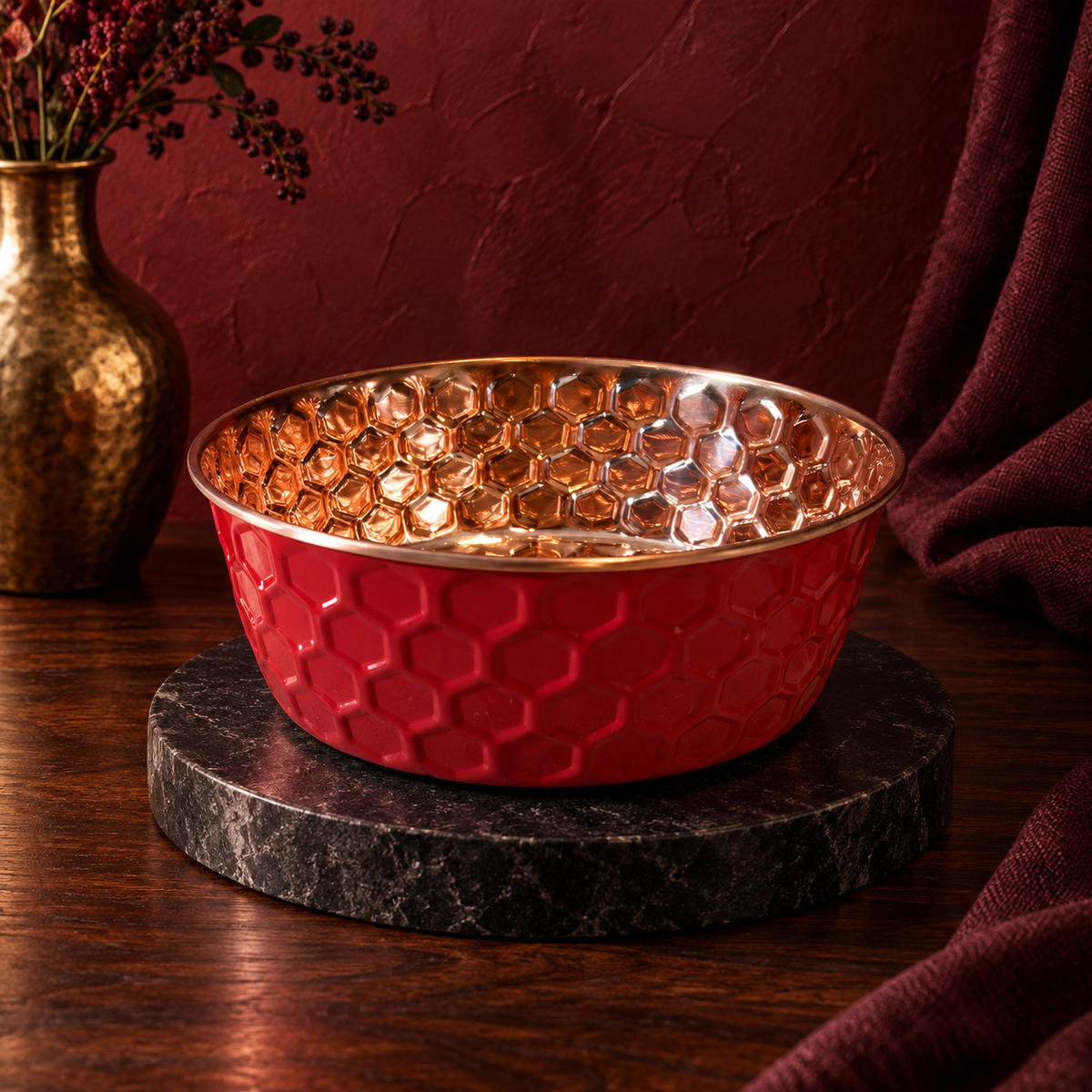 RUBY pink diamond-hammered copper pet bowl on a dark marble stand, moody red studio setting with a brass vase